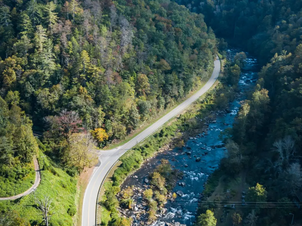 Aerial view of a winding road running alongside a rocky river and lush green forest near Tapoco Lodge.