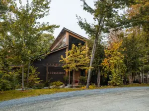 A dark wood barn-style building at one of many design-forward nature retreats, with a steep gabled roof amid autumn trees.