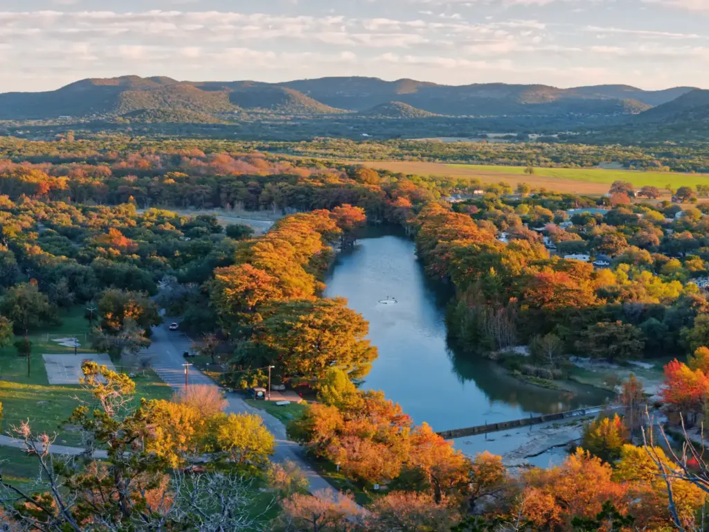 Aerial view of fall foliage along one of the best road trips in Texas, with a river winding through golden-hour hills.