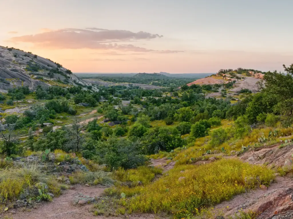Sunset view of granite hills and green scrubland at Enchanted Rock State Natural Area in Texas Hill Country.
