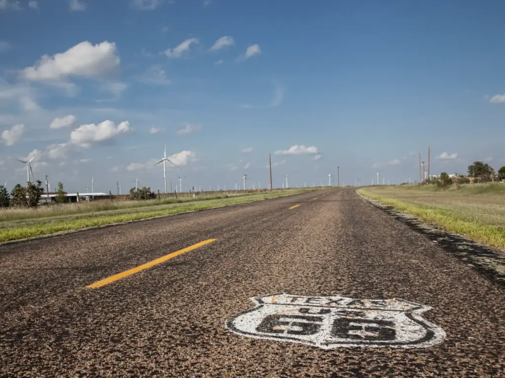 A weathered two-lane road on one of the best road trips in Texas, marked with a Route 66 shield under a partly cloudy sky.