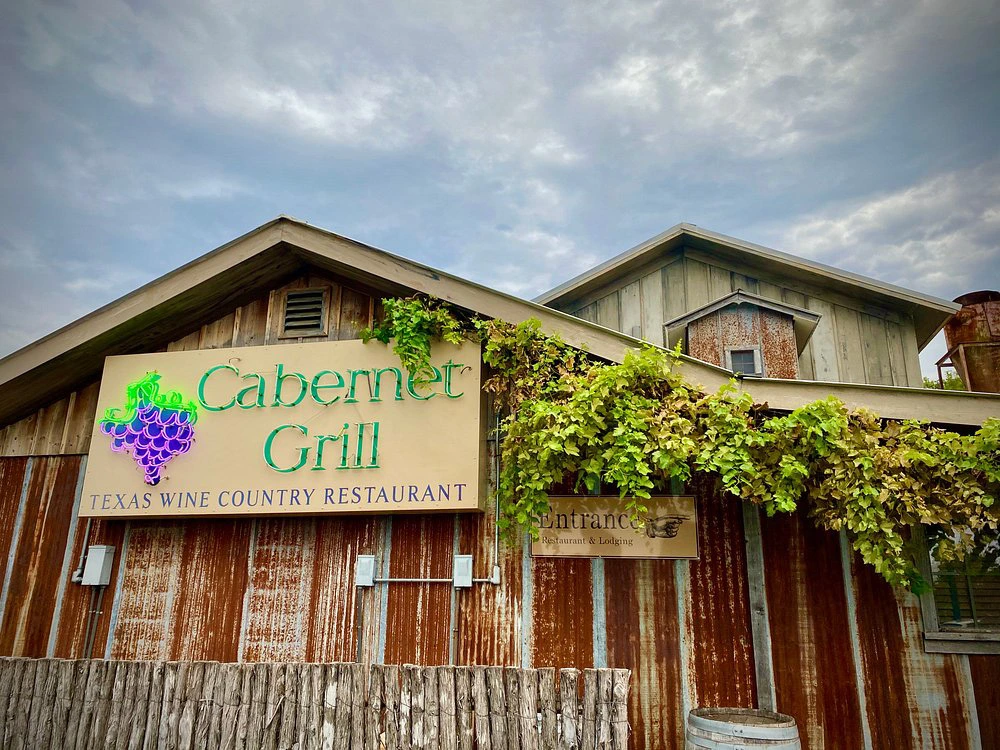 The rustic, corrugated metal exterior of Cabernet Grill Texas Wine Country Restaurant covered in green vines.