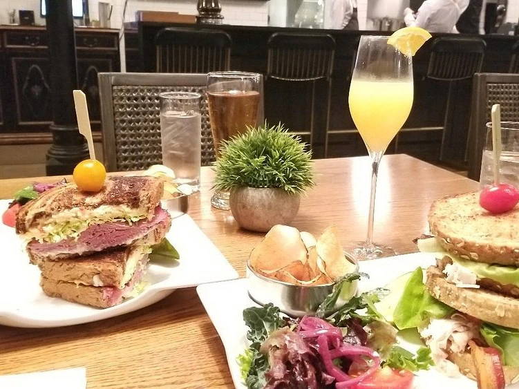 Two large sandwiches, chips, and a mimosa served on a wooden table at Vaudeville for lunch.