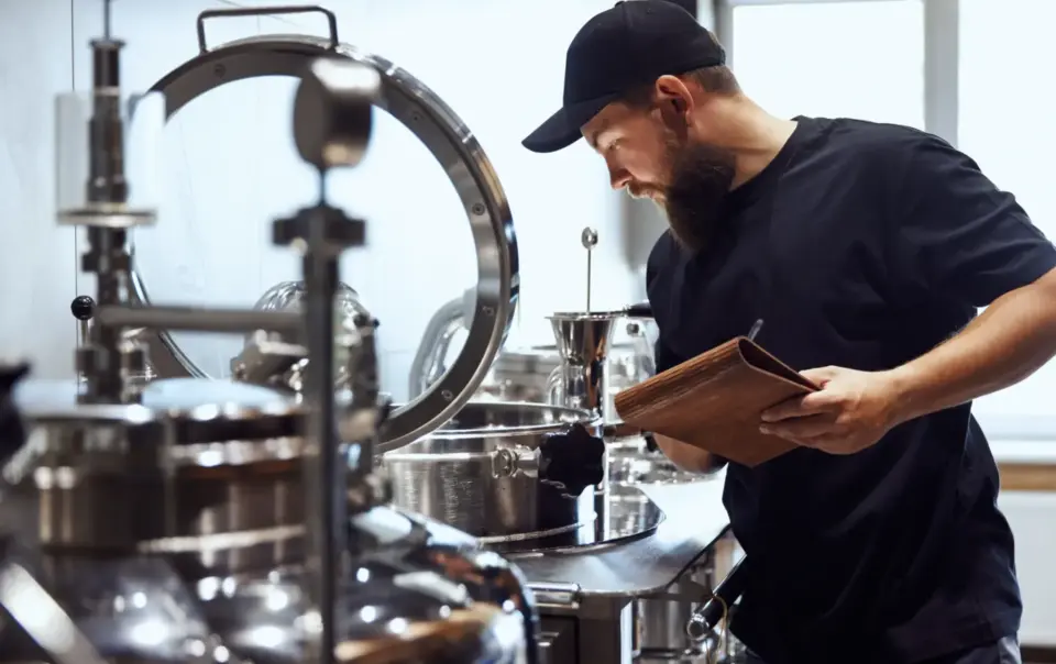 A bearded man reviews brewing notes at one of the breweries in Fredericksburg TX, inspecting stainless steel equipment.