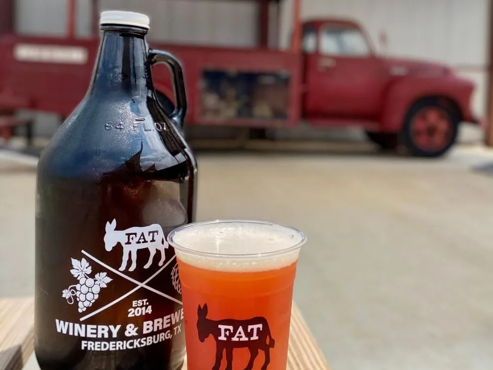 Branded growler and hazy orange beer from one of the top breweries in Fredericksburg Texas, featuring Fat Winery and Brewery logo.