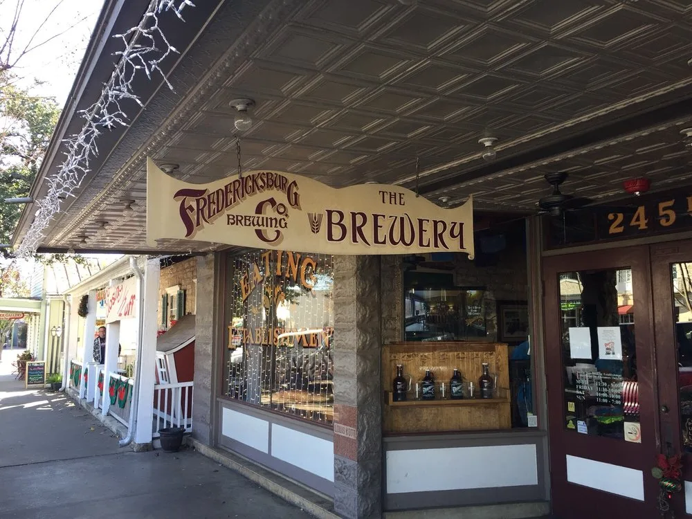 Storefront of one of the top breweries in Fredericksburg Texas, featuring a wooden hanging sign above a brick entrance.