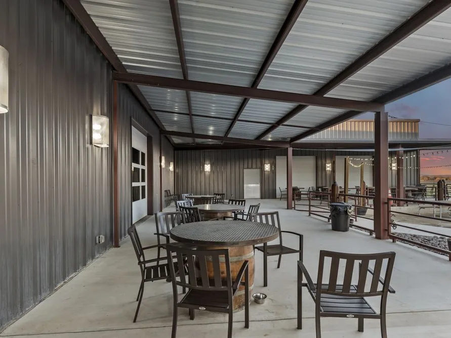 Covered outdoor patio with metal roof, round wicker tables, dark chairs, and string lights at dusk.